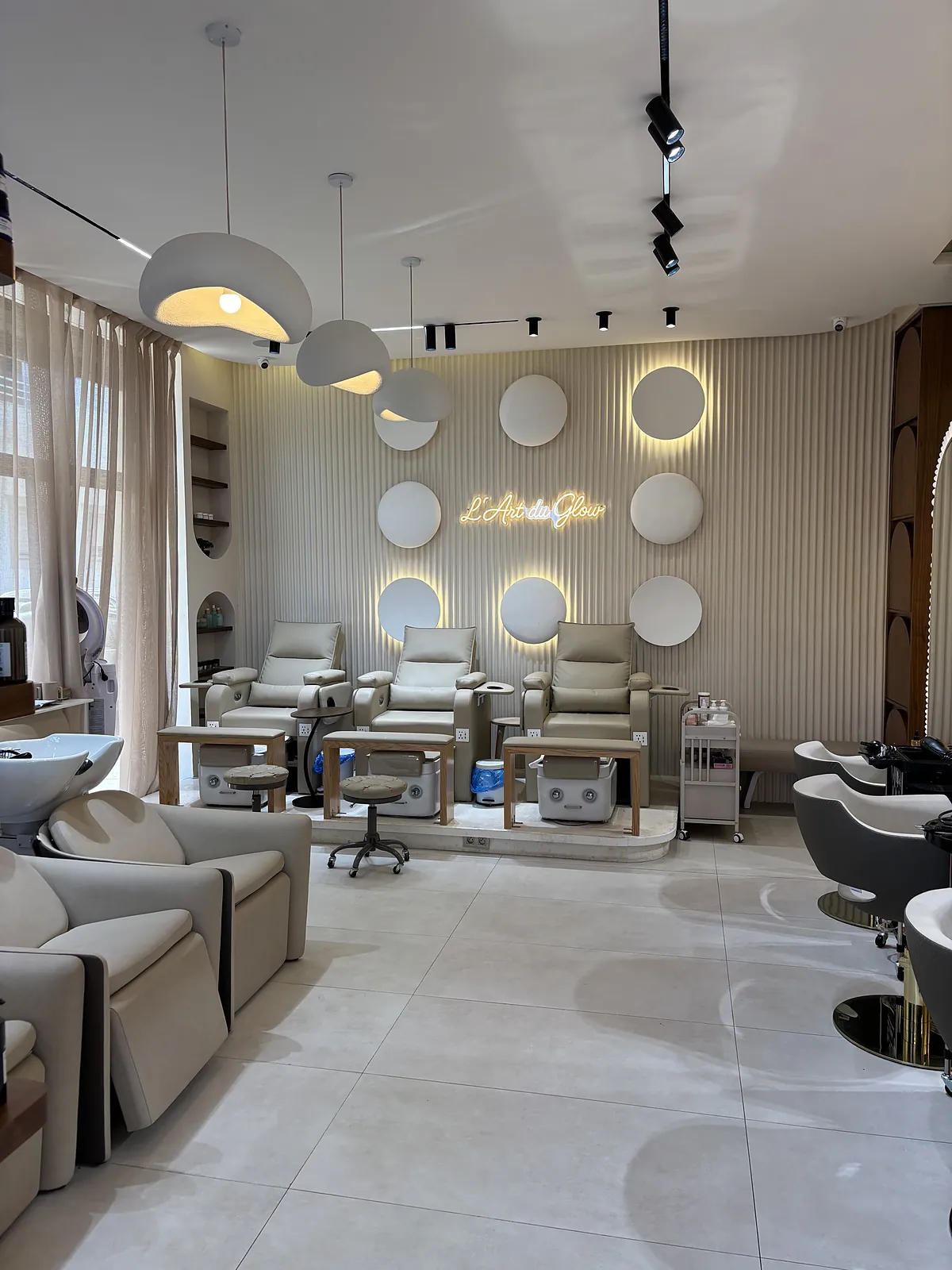 Le salon en entier : les bacs, les fauteuils de pédicure devant le mur lumineux, et les miroirs en arche