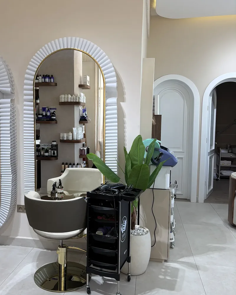 Un poste de coiffure devant un miroir en arche, avec les étagères de produits et les portes en arche du salon