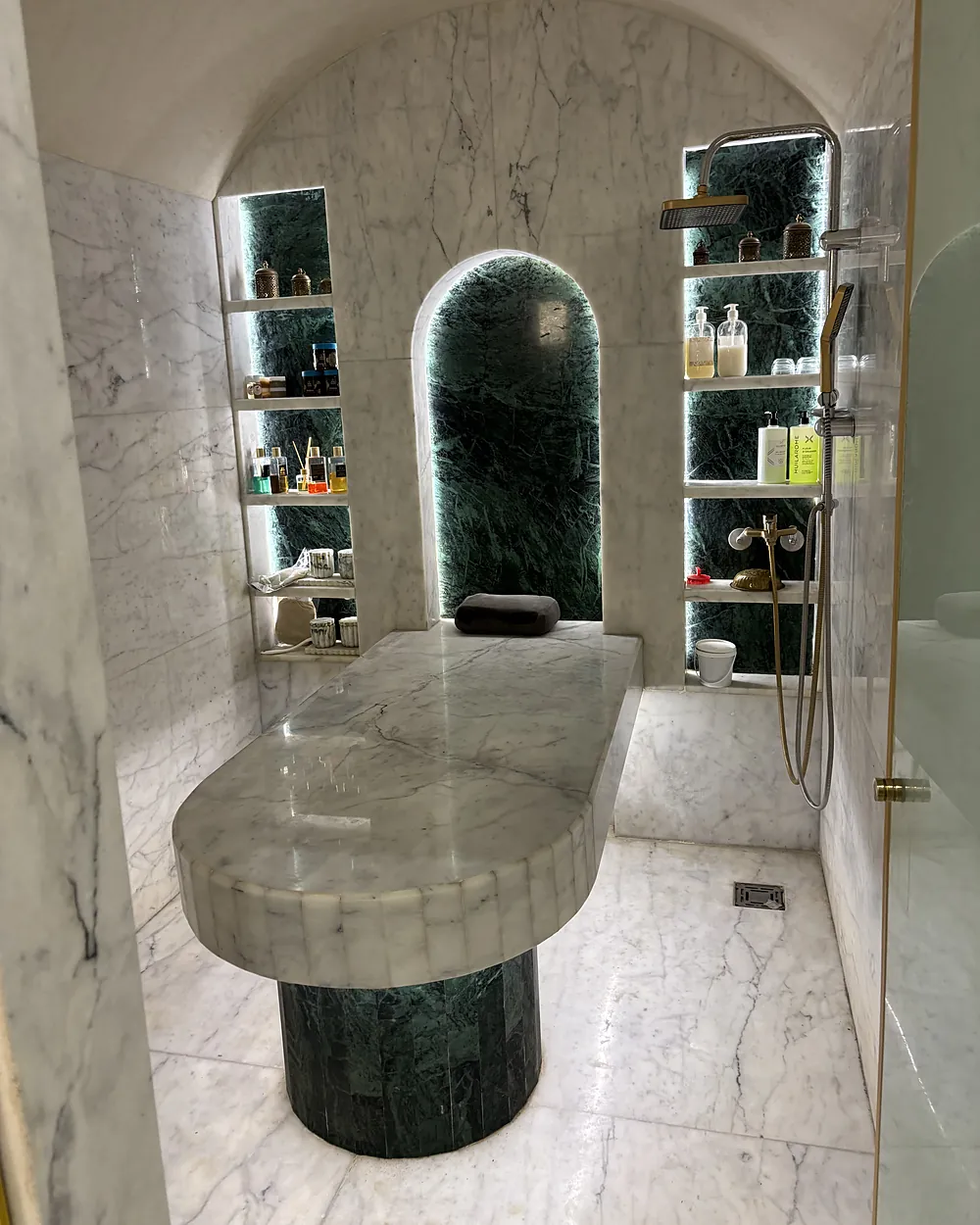 Le hammam : la table de gommage en marbre blanc sur un pied de marbre vert, sous une arche éclairée